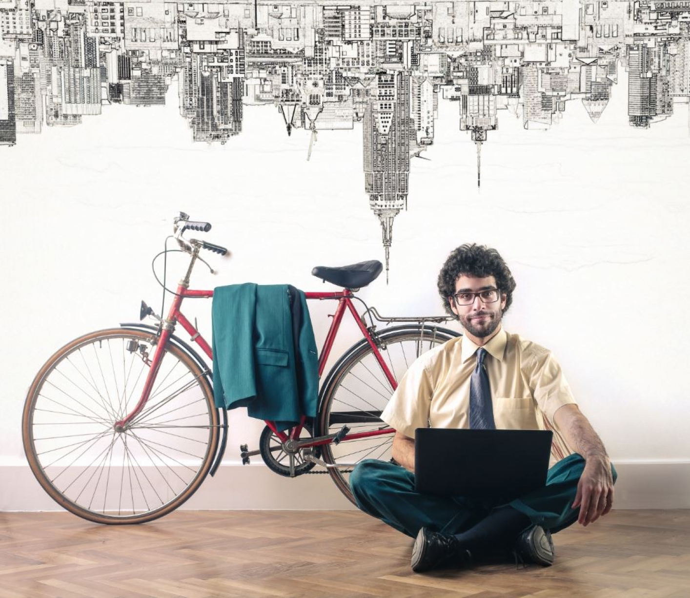 Een man werkt thuis op zijn laptop met op de achtergrond zijn racwfiets en op het behang staat de skyline van een stad op zijn kop afgebeeld