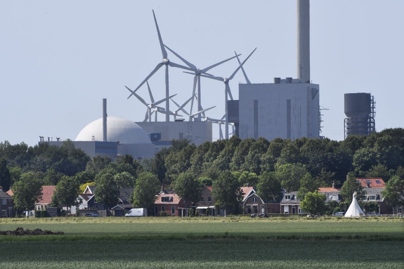 windmolens en kerncentrale met huizen en weiland op de voorgrond 
