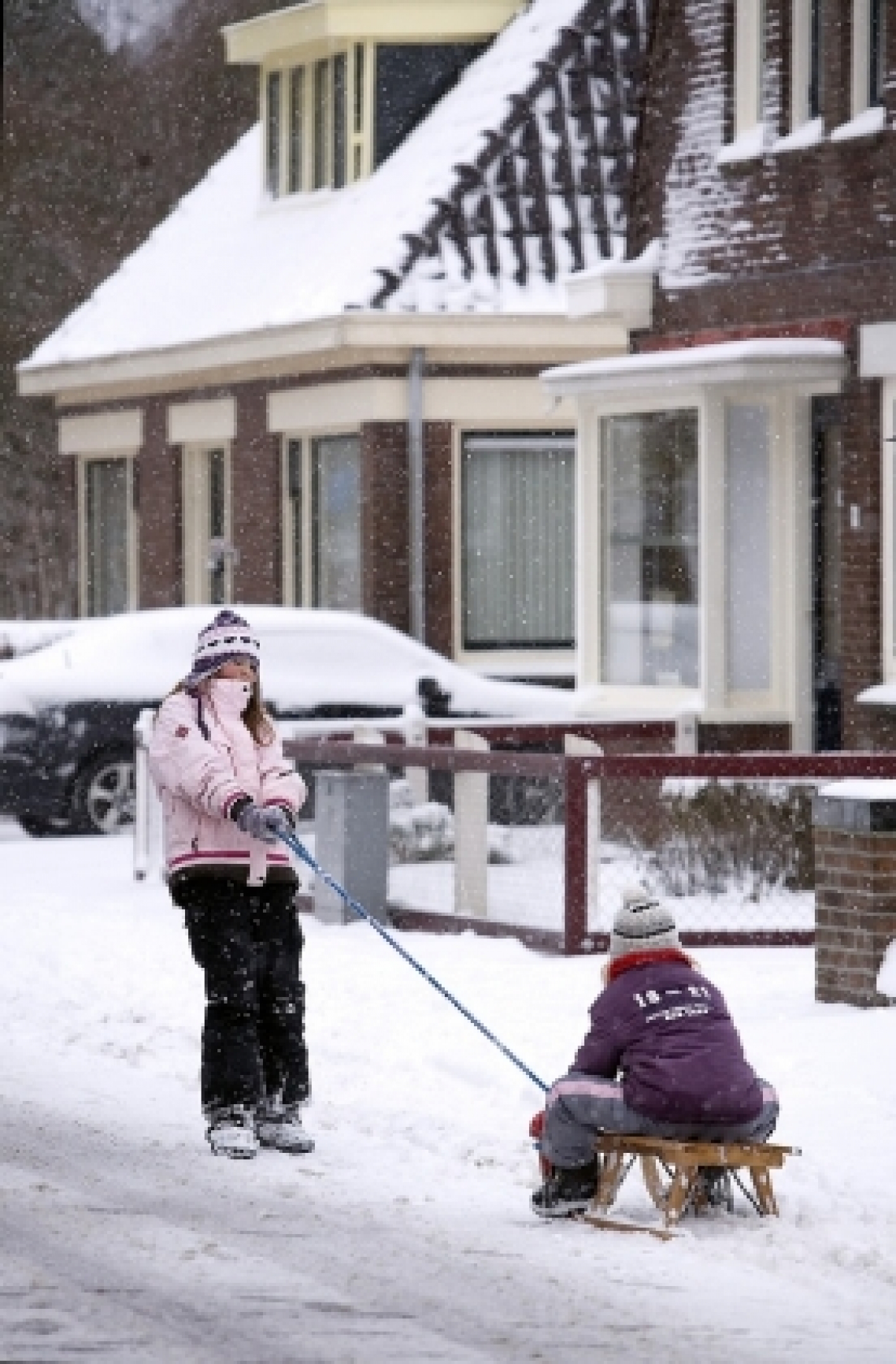 kinderen spelen met een sleetje in de sneeuw in een woonwijk
